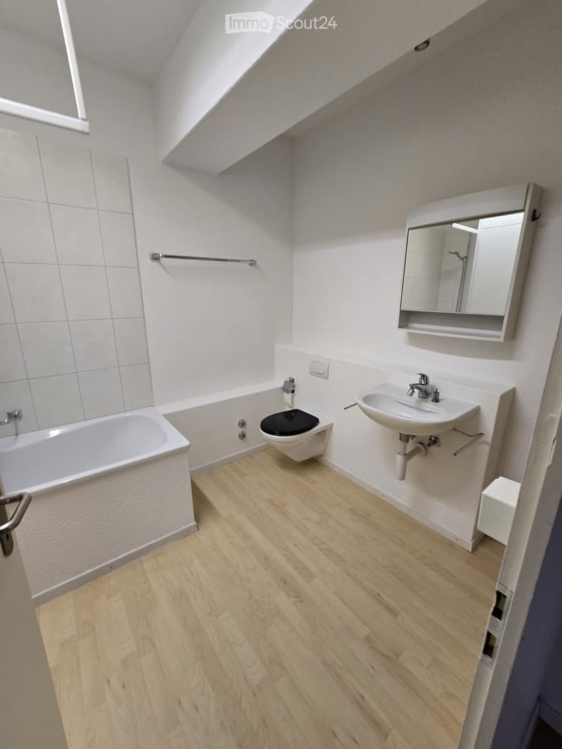 Modern bathroom with wooden flooring, white tiled walls, bathtub, toilet, sink, and a mirror cabinet.