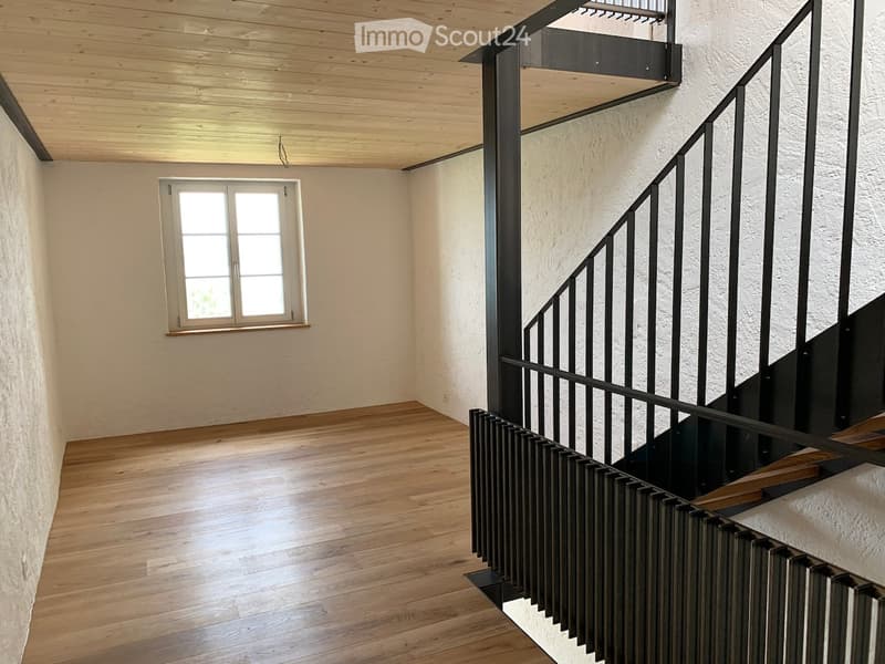 Empty hallway with wooden flooring, white walls, and a window on one side. A modern metal staircase leads upwards.