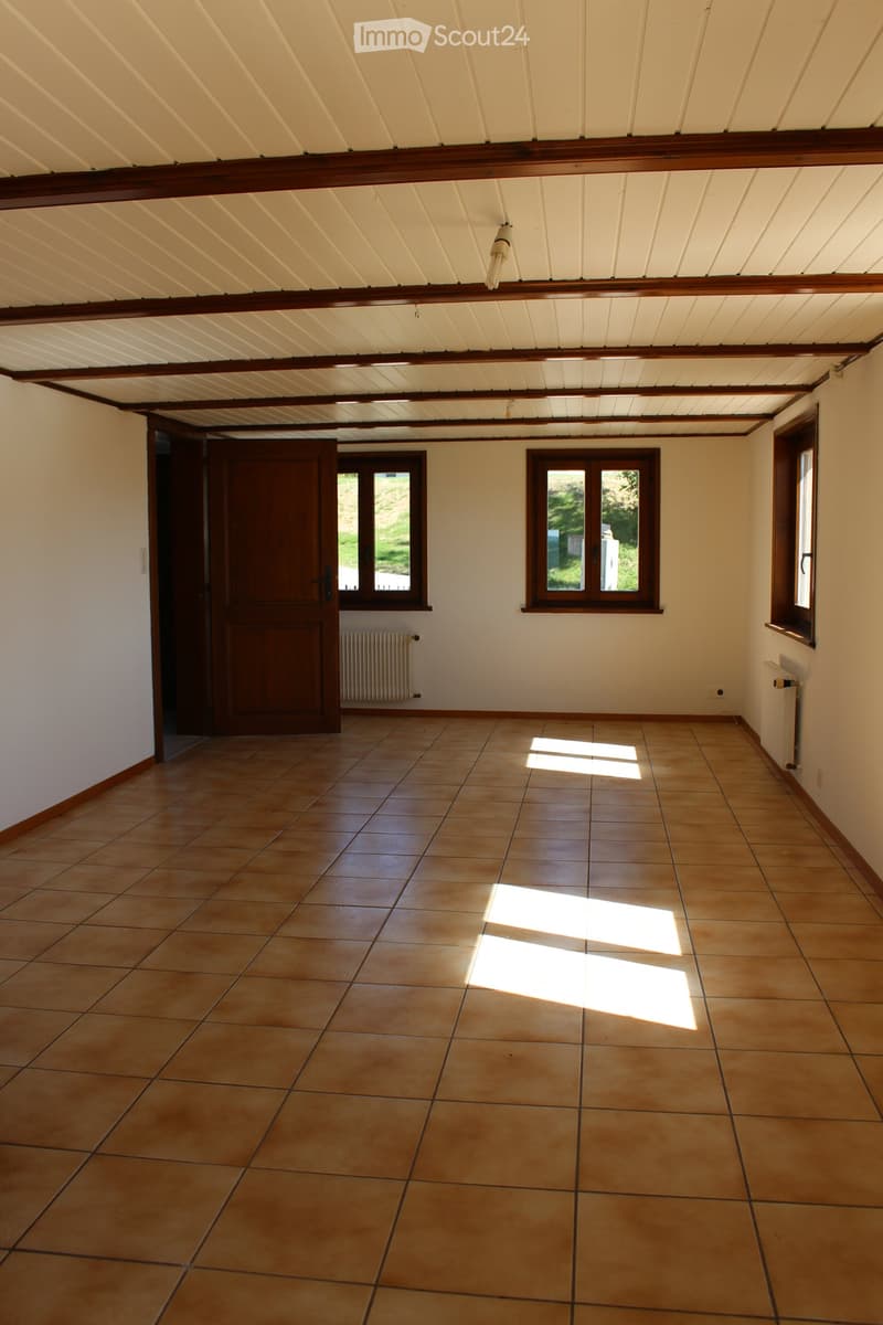 Empty room with tiled floor, white walls, wooden door, and windows letting in natural light.