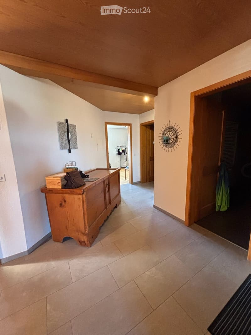 Bright hallway with tiled floor, wooden chest, artwork, and open doors leading to other rooms.