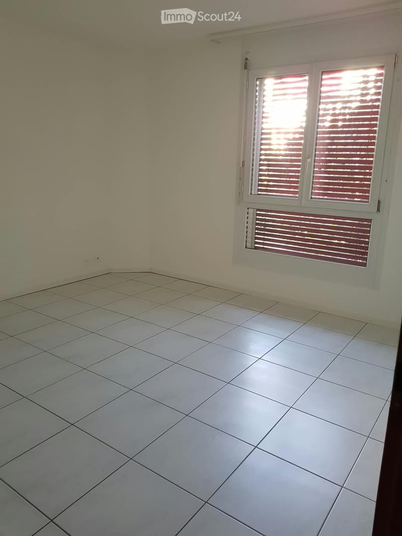 Empty room with tiled floor and white walls, featuring a window with blinds and a radiator below it.
