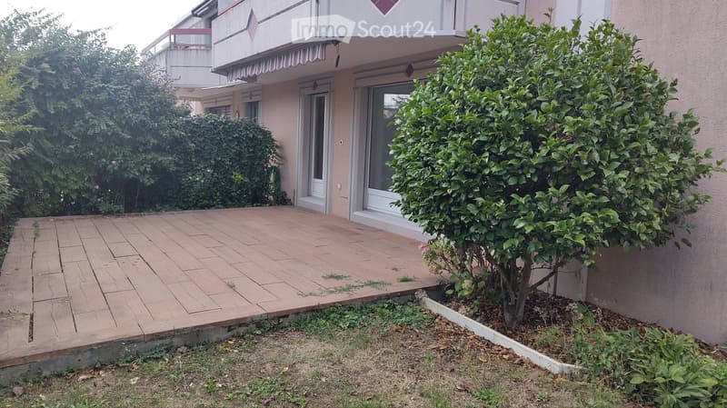 Brick patio area adjacent to a building with a small tree and surrounding greenery.