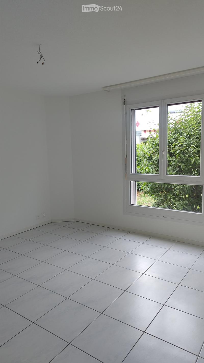 Empty room with white tiled floor and white walls, featuring a large window with white frame and blinds, allowing natural light to enter.