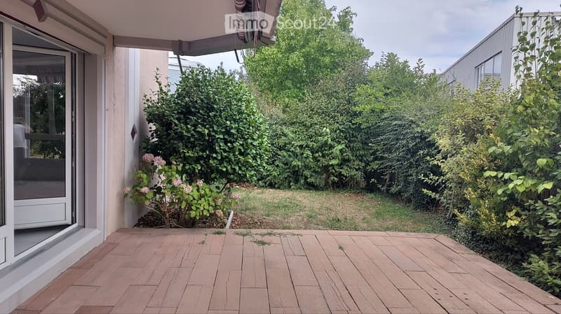 Wooden deck area with surrounding greenery and a view of a building in the background.