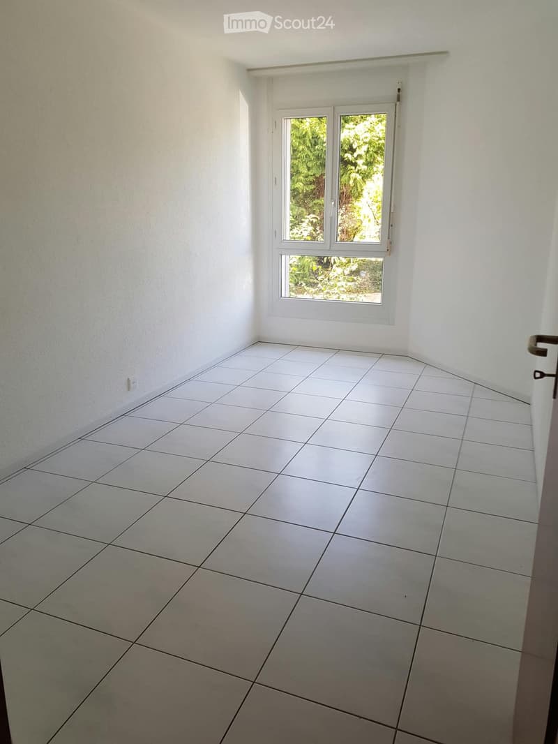 Empty room with white tiled floor and white walls, featuring a window with white frame and a door with a silver handle.