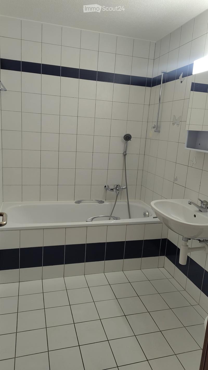 Bathroom with white tiled walls and floor, featuring a bathtub, sink, and showerhead.