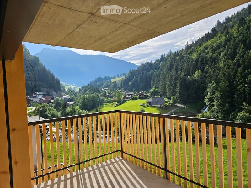 Balcony with wooden railing and a scenic view of a valley, mountains, and a small village.