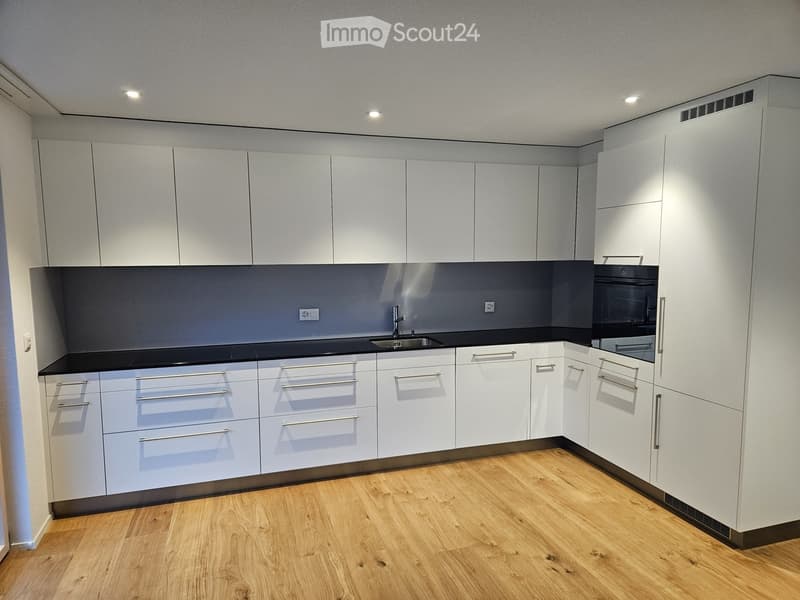 Modern kitchen with white cabinets, black countertops, and wooden flooring.