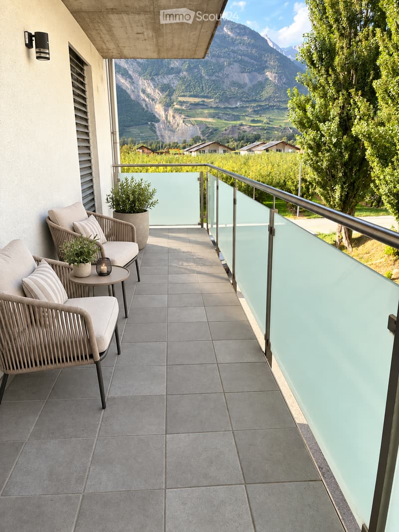 Balcony with a scenic mountain view, featuring a wicker chair, small table, and potted plants.
