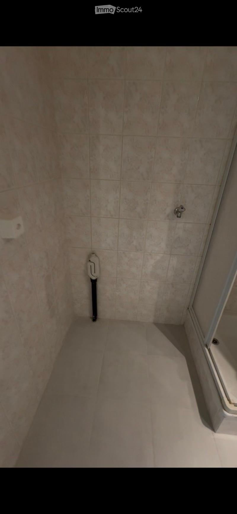 Empty bathroom with tiled walls and floor, a showerhead, and a toilet visible in the corner.