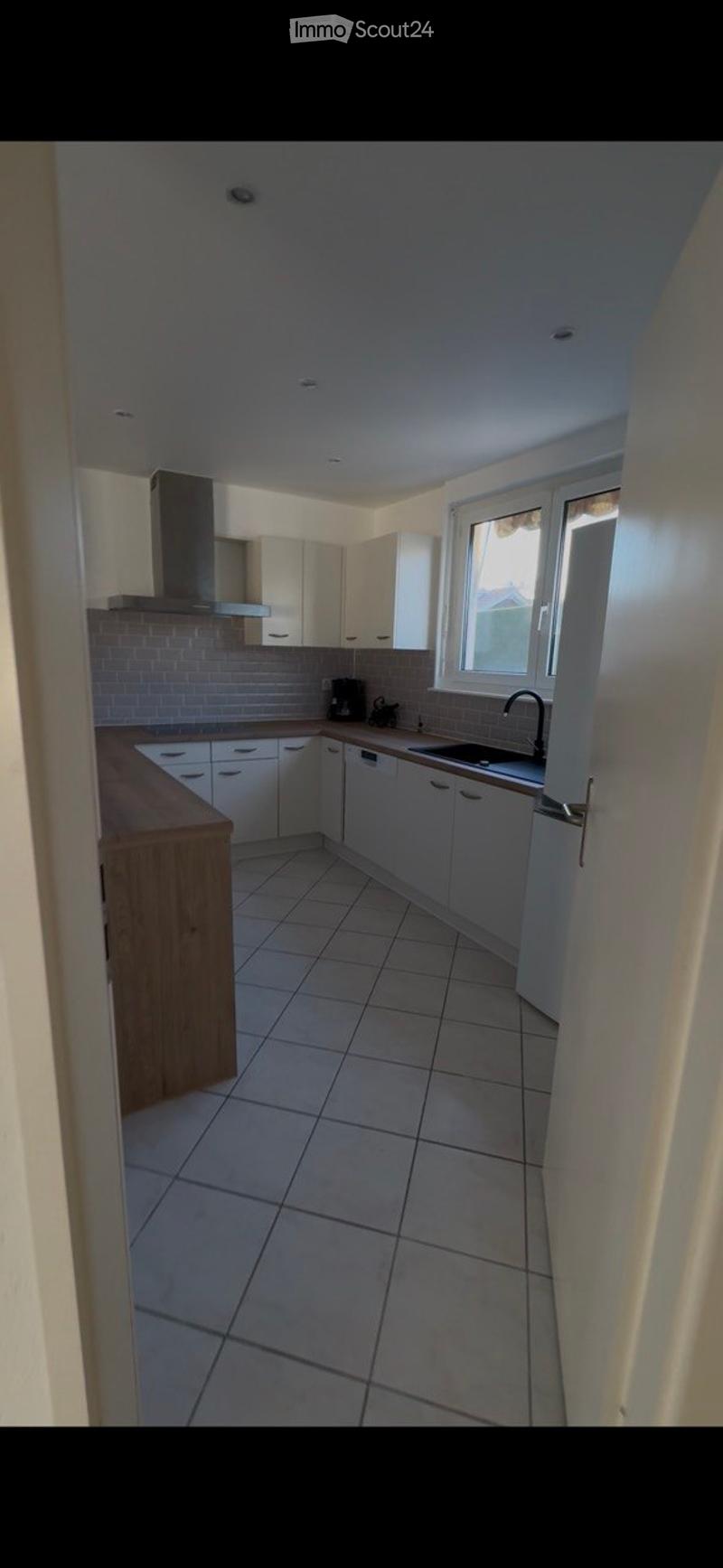 Modern kitchen with white cabinets, tiled floor, and a wooden countertop. Features include a sink with a faucet, a dishwasher, and a coffee maker on the counter.