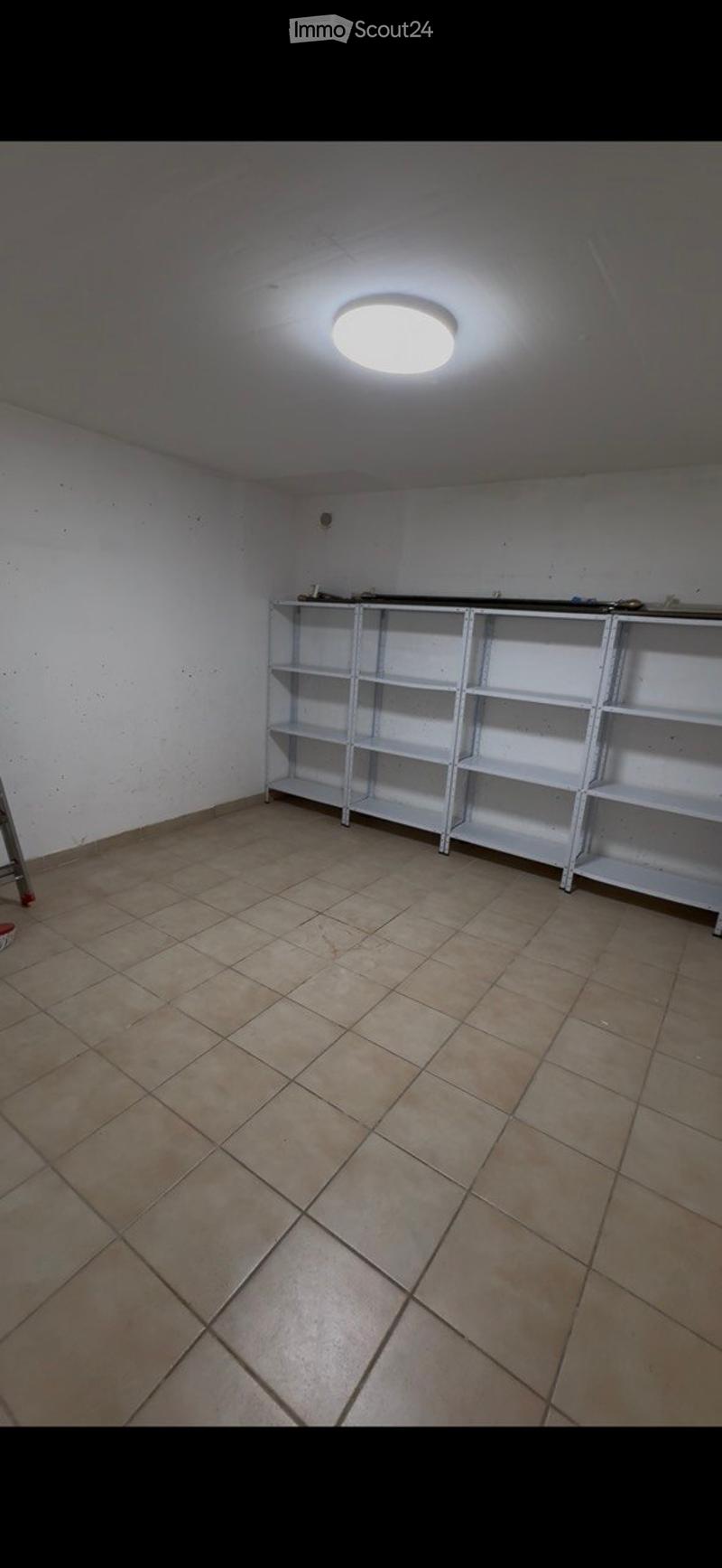 Empty room with tiled floor, white walls, and a metal shelving unit against one wall. The room is unfurnished and appears to be a storage or utility space.