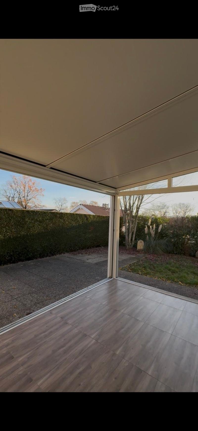 Empty room with wooden flooring and large sliding glass doors leading to an outdoor area with a paved driveway and garden.