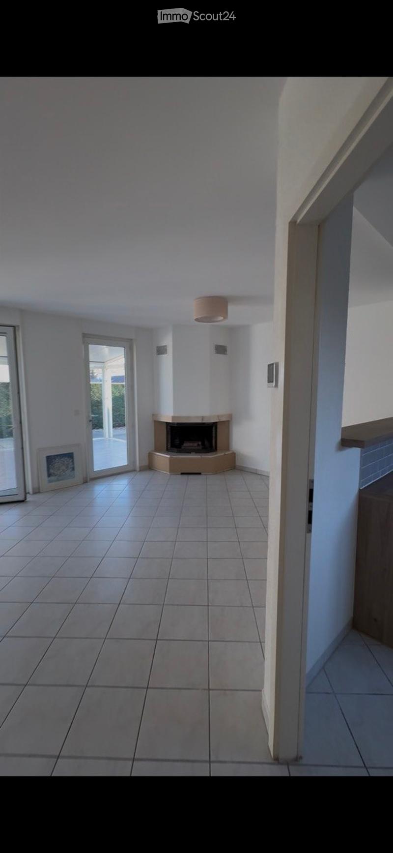 Empty living room with tiled floor, fireplace, large glass door leading to outdoor area, and white walls.