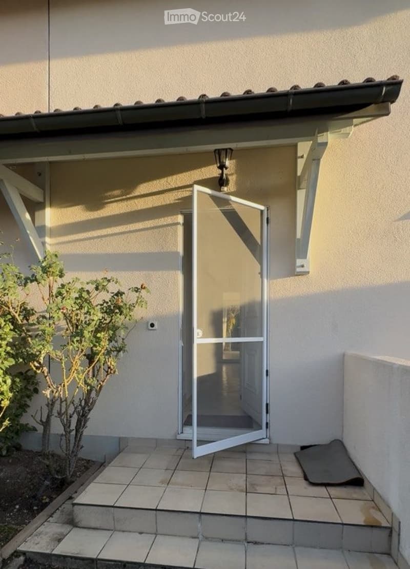 Balcony with tiled floor, open sliding glass door leading to interior, small plant on left, light fixture above door.