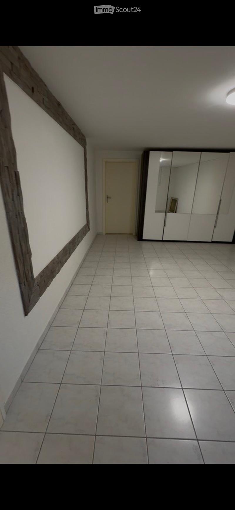 Empty hallway with tiled floor, white walls, a closed door, and a mirrored wardrobe unit.