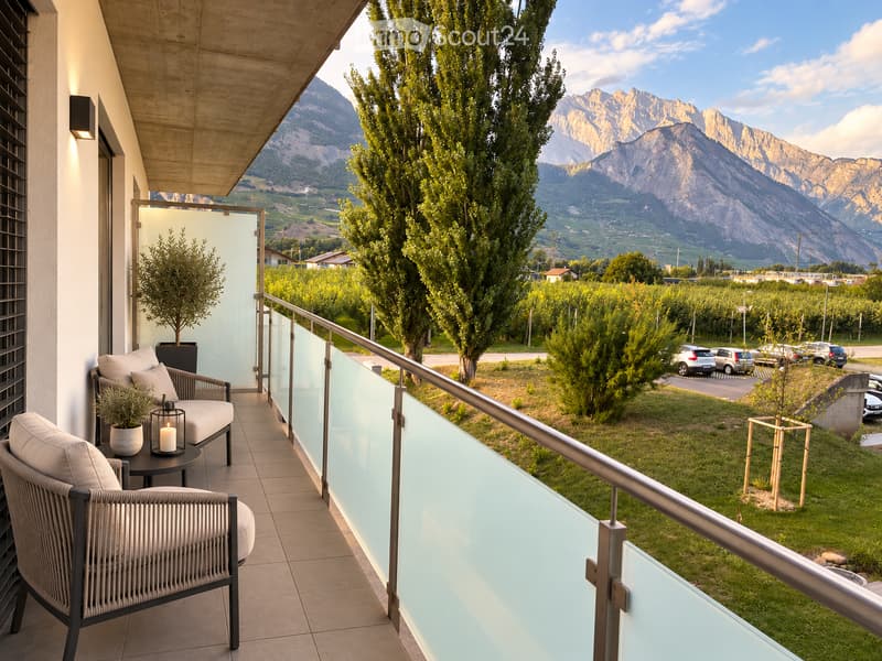 Balcony with modern furniture, including two chairs and a small table, overlooking a scenic valley and mountains.