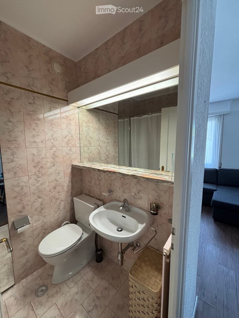 Modern bathroom with marble tiles, a toilet, a sink with a faucet, a mirror, and a cup on the sink counter.