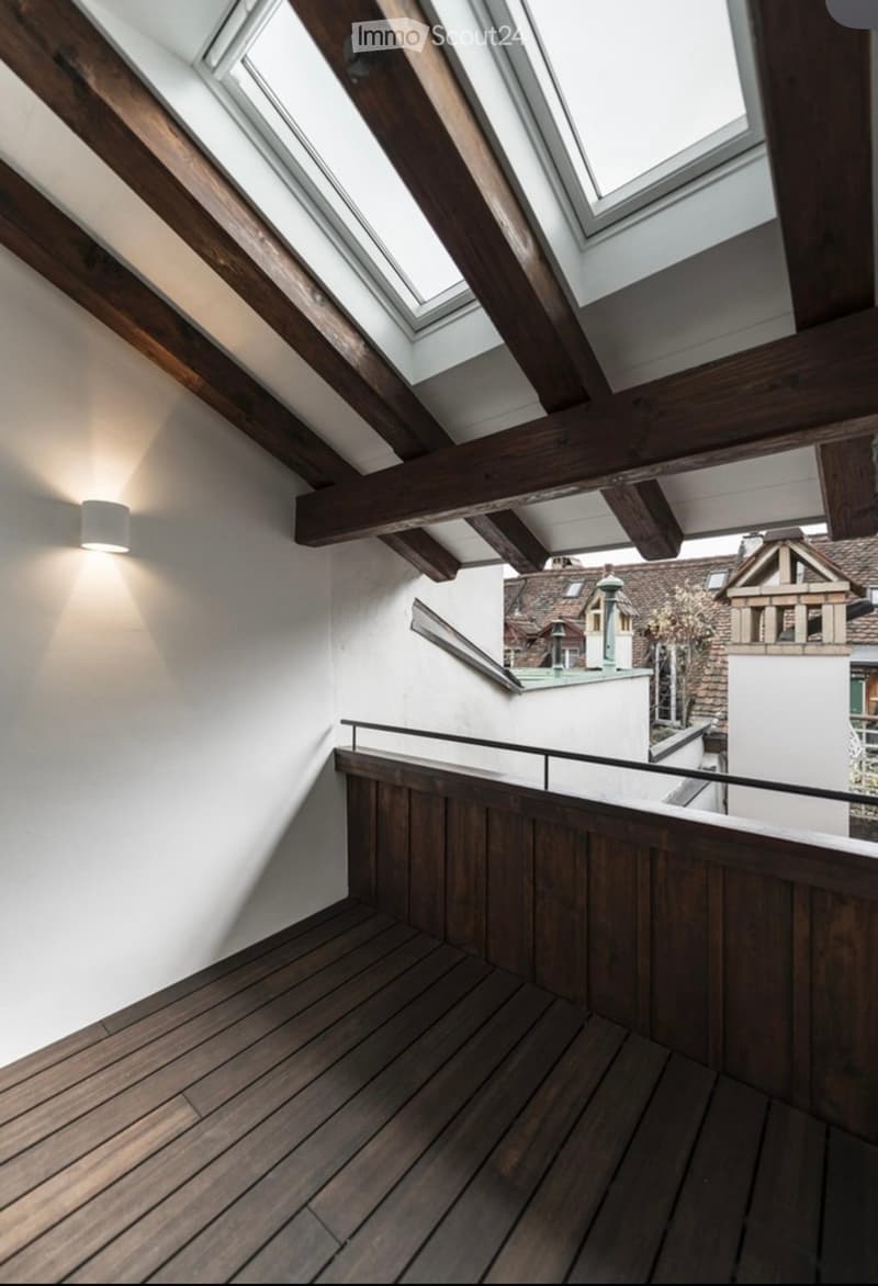 Wooden hallway with exposed beams, skylights, and a view of the cityscape through a glass railing.