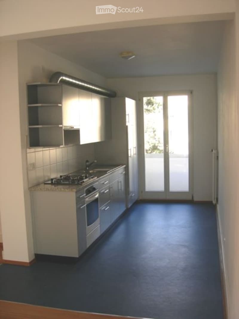 Modern kitchen with white cabinets, stainless steel appliances, dark blue flooring, and a sliding glass door leading to a balcony.
