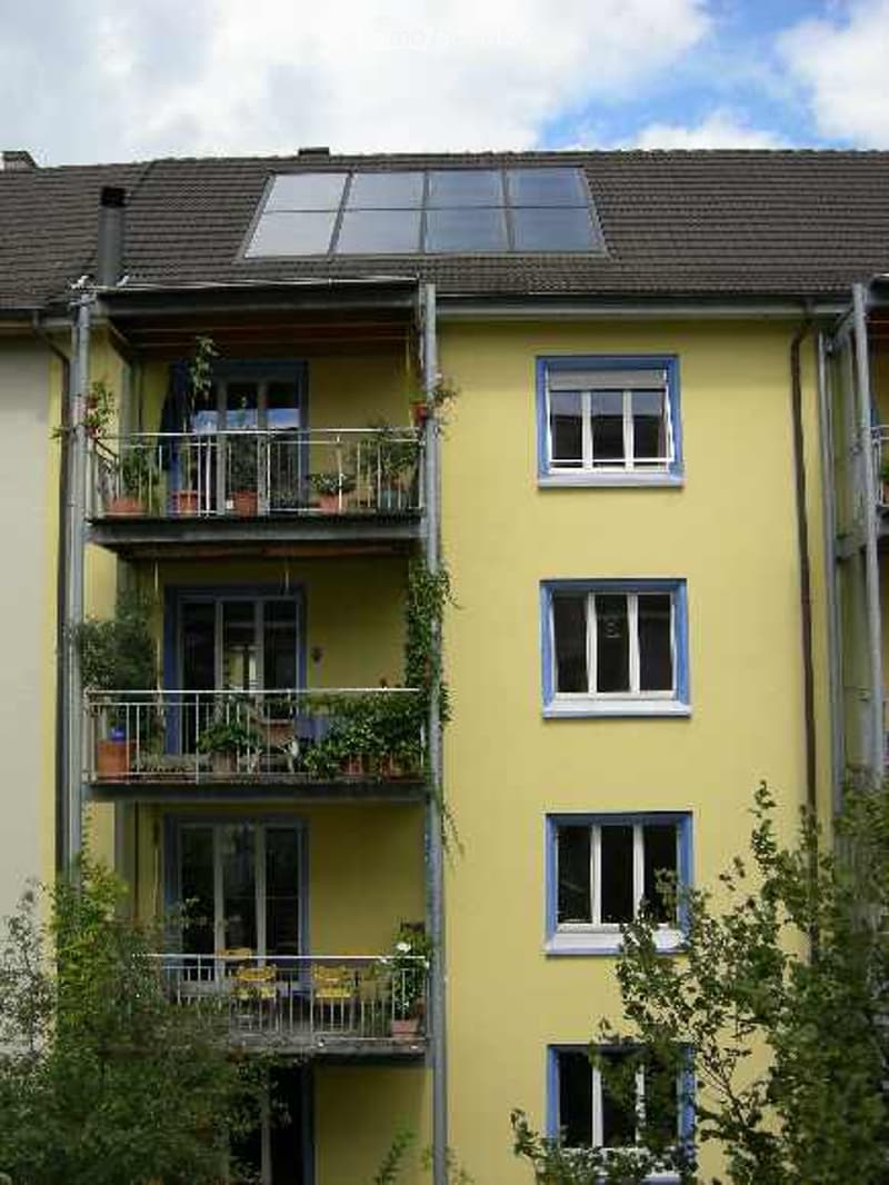 Yellow apartment building with multiple balconies, each decorated with potted plants and outdoor furniture.