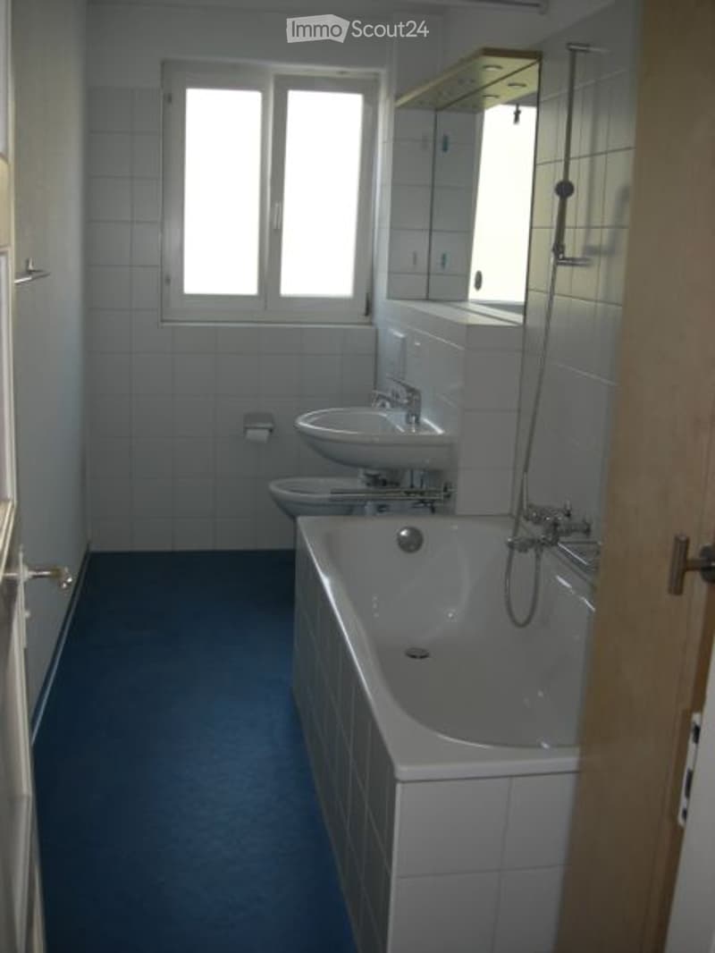 Modern bathroom with white tiles, blue flooring, bathtub, sink, toilet, and mirror.