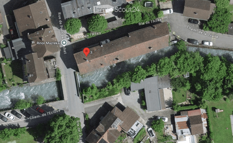 Aerial view of a residential area showing multiple buildings with red-tiled roofs, surrounded by greenery and streets.