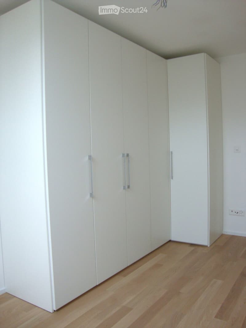 Empty room with light-colored wooden flooring and white built-in wardrobes with silver handles.