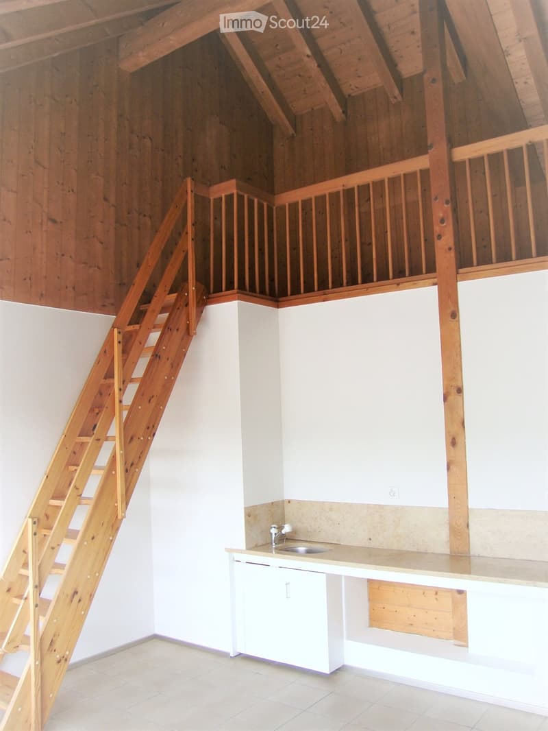 An unfurnished room with a wooden staircase leading to an attic space, a small white countertop with a sink, and light-colored tiled flooring.