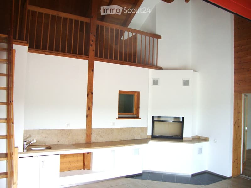 Modern kitchen with white cabinets, a sink, and a built-in fireplace. The space features wooden beams and a lofted upper level with a wooden railing.