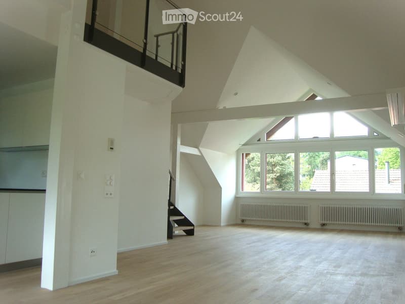 Bright, empty room with wooden flooring, white walls, large windows, and a staircase leading to an upper level.