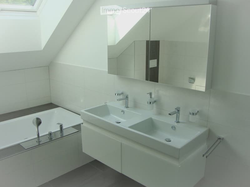 Modern bathroom with a large mirror, double sink, bathtub, and sleek chrome fixtures.