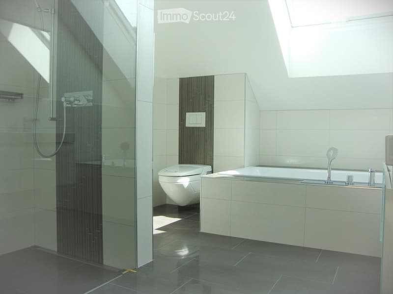 Modern bathroom with a bathtub, toilet, and glass-enclosed shower area. The space features dark tiled floors and walls, with a sleek, contemporary design.