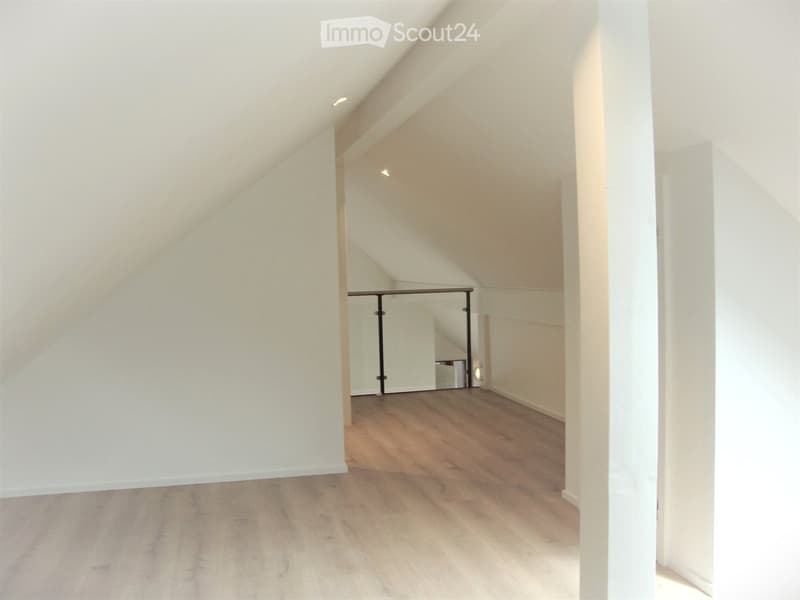 Empty attic space with wooden flooring, white walls, and exposed beams. No furniture or equipment present.