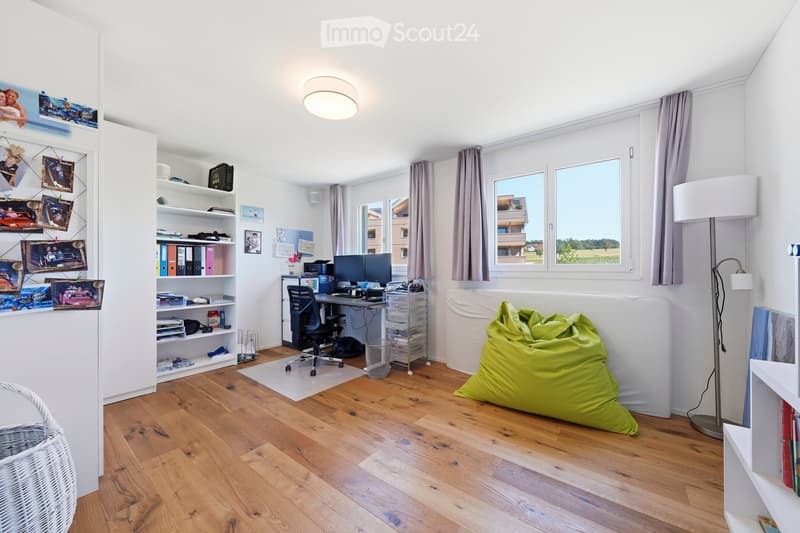 Bright room with wooden flooring, large windows, a desk with a computer, a bean bag chair, a bookshelf, and a wicker basket.