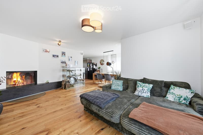 Modern living room with a grey sectional sofa, ottoman, coffee table, fireplace, and a dining area with a table and chairs.