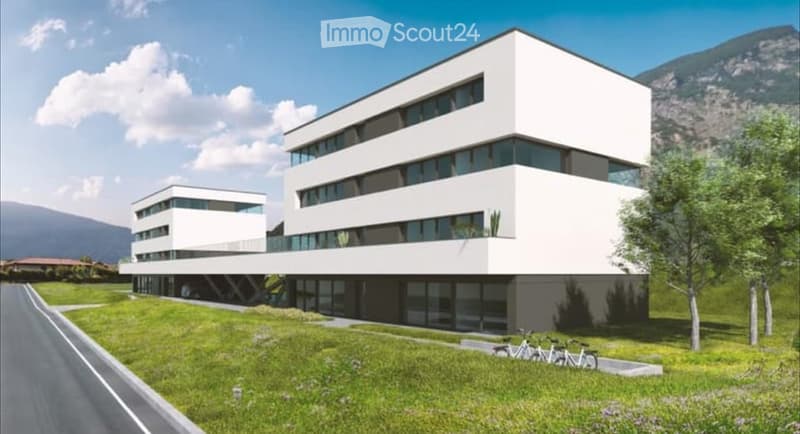 Modern, multi-story white building with large windows and a sleek design, surrounded by a green lawn and trees.