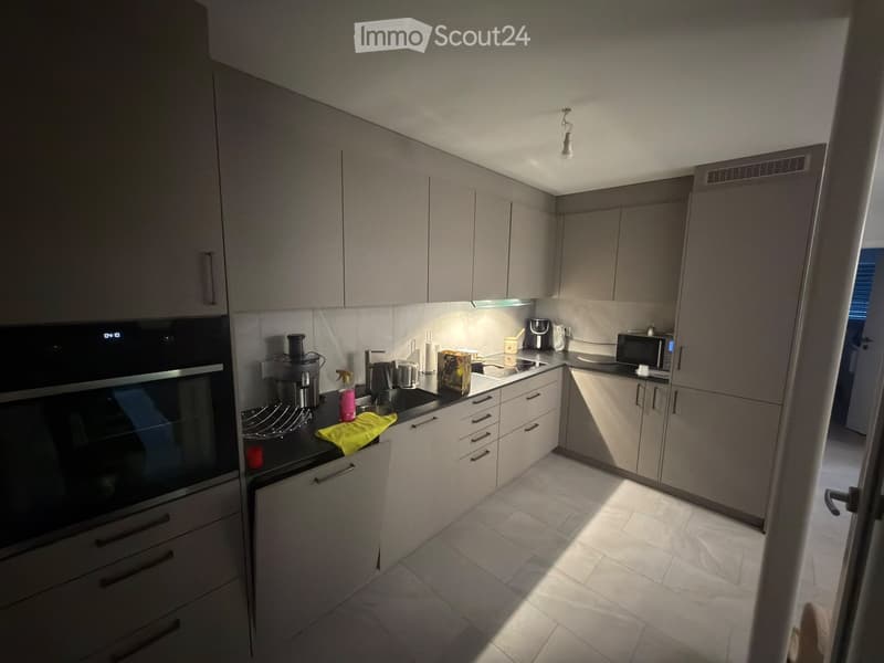 Modern kitchen with light grey cabinets, stainless steel appliances, and a black countertop. Visible items include an oven, microwave, coffee maker, and various kitchen tools.