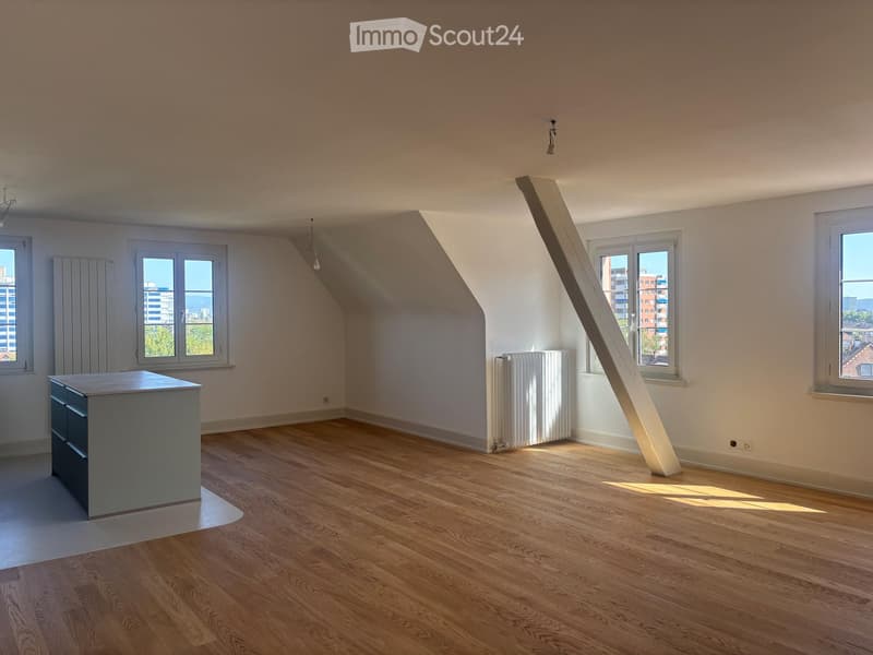 Empty room with wooden flooring, white walls, and multiple windows letting in natural light. A radiator is visible near one window, and a small cabinet is placed against the wall on the left side.