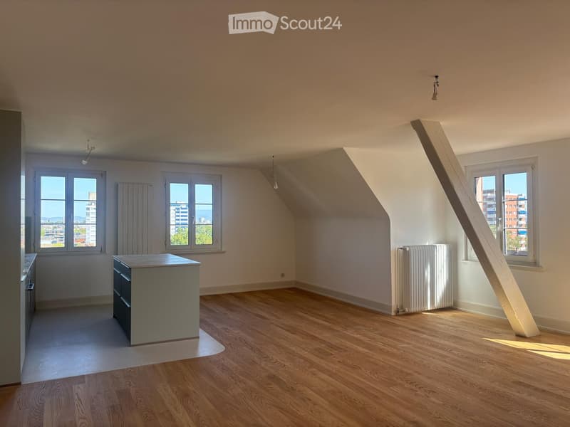 Empty room with wooden flooring, white walls, and large windows offering a city view. There is a radiator and a small cabinet visible.