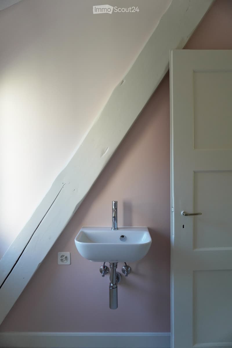 Compact bathroom with a white sink and modern chrome faucet, installed under a sloped ceiling with soft pink walls.