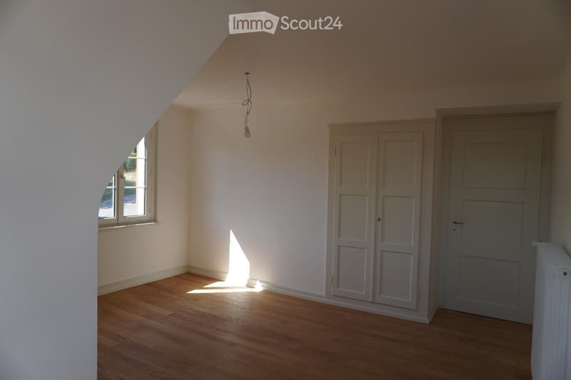 Empty room with wooden flooring, white walls, built-in closet, and a window letting in natural light.