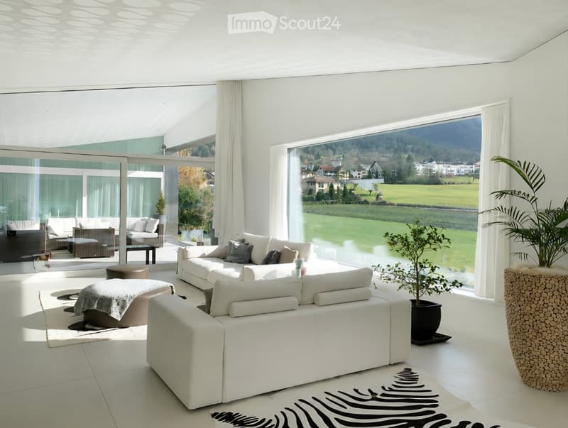 Modern living room with large windows offering a scenic view, white sofa, ottoman, small table, and decorative plants.