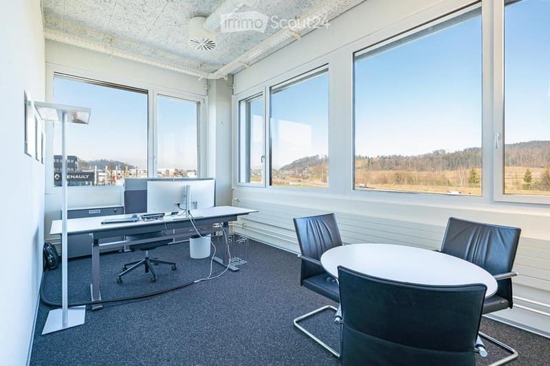 Modern office space with large windows, a desk with a computer, chairs around a round table, and a floor lamp.