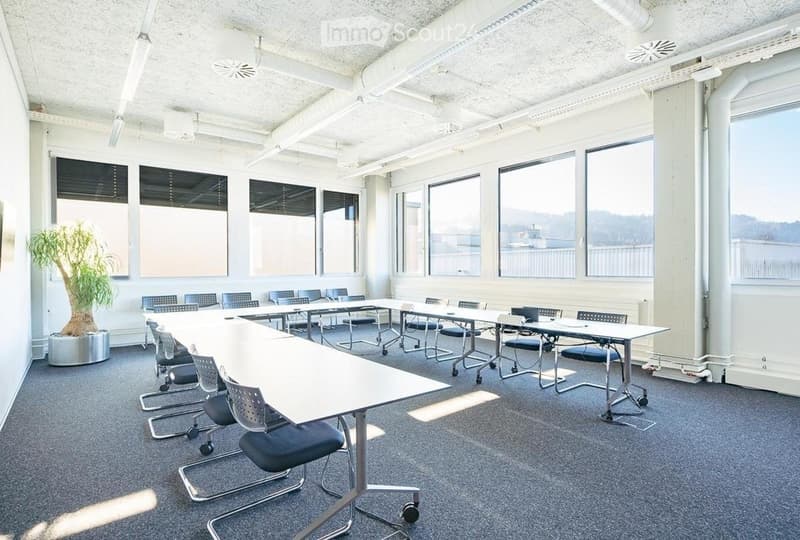 Modern conference room with long tables, chairs, laptops, and a potted plant near the window.