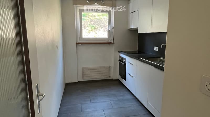 Modern kitchen with white cabinets, a sink, and an oven. Features a window with a view of greenery, a radiator, and tiled flooring.