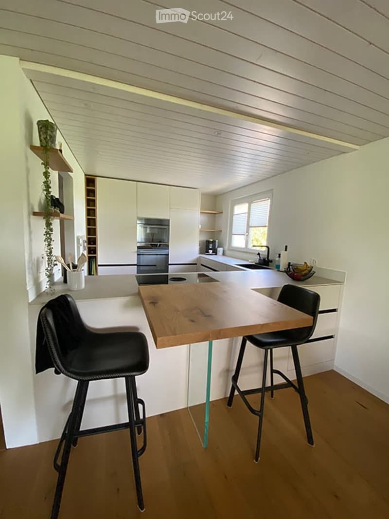 Modern kitchen with white cabinets, wooden table, black stools, and a sleek sink area.