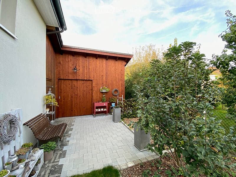 Outdoor patio area with a wooden bench, small table, potted plants, and a wooden shed.