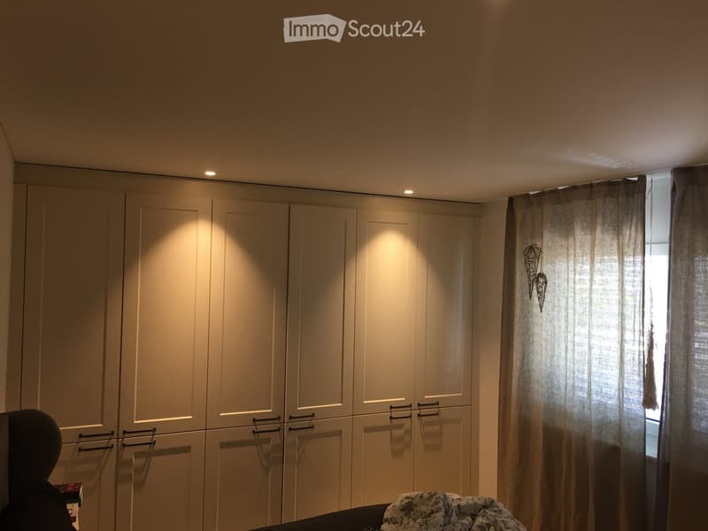 Bedroom with large built-in wardrobe, window with curtains, and a bed with a patterned blanket.