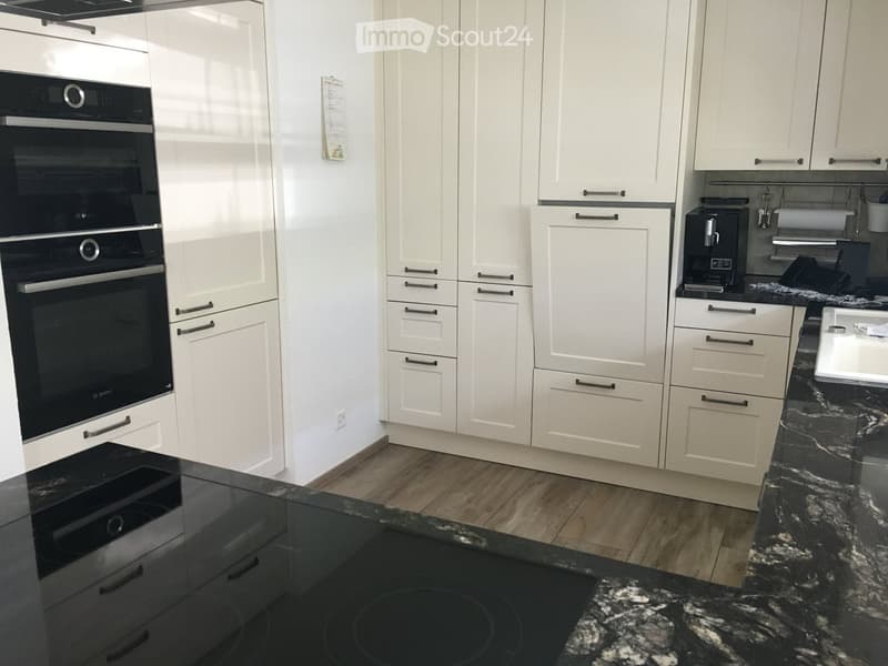 Modern kitchen with white cabinets, black granite countertops, and stainless steel appliances including an oven and coffee maker.